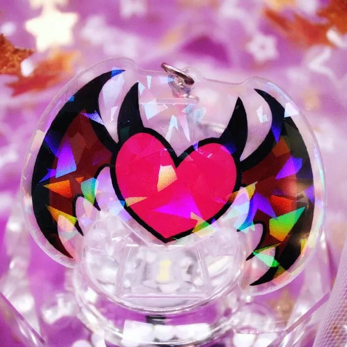 A heart shaped acrylic charm with wing and horn on it.