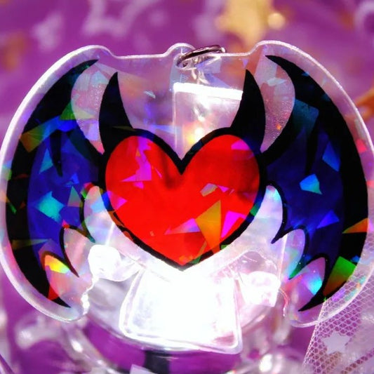 A heart shaped acrylic charm with wing and horn on it.