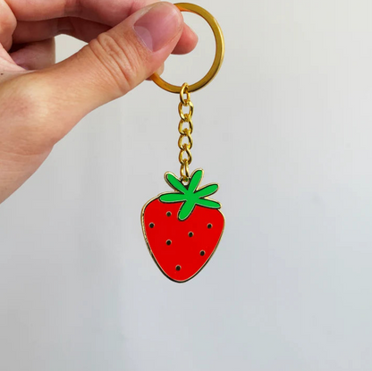 A hand holding a strawberry hard enamel keychain